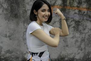 Gorgeous strong young asian woman with whute shirt showing biceps and smiling. Indonesian girl strong concept. photo