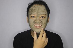 el hombre asiático sonriente estaba feliz con la cámara cuando usaba una máscara facial de belleza foto