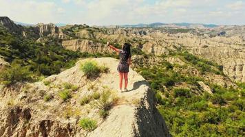 drone girato giovane donna caucasica in piedi sulla cima della montagna. turista che utilizza lo smartphone per selfie insieme al punto di vista. concetto di ripresa aerea, natura, viaggi e avventura. video