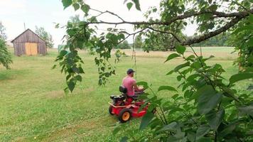statische hd-opnames persoon zit op rode grasmaaier en maait gras op achtertuin op het platteland van litouwen video