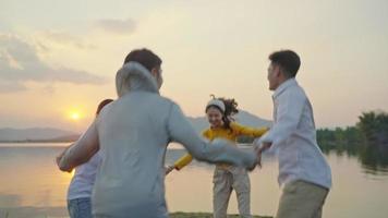 gruppo quattro persone amici uomini e donne asiatici picnic in campeggio che celebrano tenendosi per mano in cerchio e ballando divertendosi e godendosi la tenda a terra. area del serbatoio durante le vacanze al tramonto. video