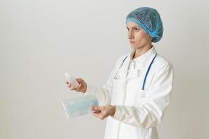 Female doctor in medical mask and uniform offers mask and disinfectant in bottle photo