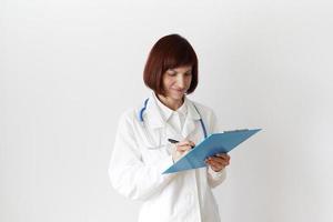 Female adult doctor stands on white background. Beautiful woman, thinking, writing photo