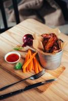 harnished chicken wings with sauce and vegetables on wooden table photo