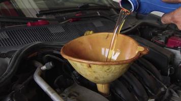 verser de l'huile neuve dans le moteur de la voiture à partir d'un récipient en plastique bleu dans les images de l'atelier de réparation. video