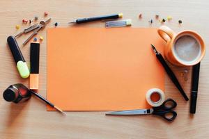 Orange empty sheet with lots of stationery objects makes photo