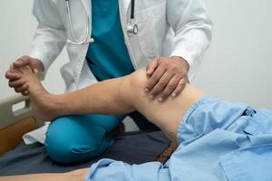 Asian doctor physiotherapist examining, massaging and treatment knee and leg of senior patient in orthopedist medical clinic nurse hospital. photo