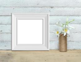 Square Vintage White Wooden Frame mockup near a bouquet of lilies stands on a wooden table on a painted white wooden background. Rustic style, simple beauty. 3d render. photo