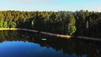 círculo aéreo ao redor do pescador com vara de pescar pescando em barco verde no cênico lago rural lituano