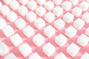 azúcar refinada sobre fondo rosa. cubos de azúcar dulce y blanco en forma geométrica. sombras duras. foto