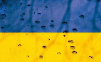 Ukrainian flag with bullet holes on the facade of a residential building as a background. Flag of Ukraine. Stop the war. Armed conflicts. Defund the armies. No to war. photo