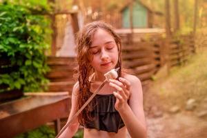 Girl eats marmellou cooked on a campfire on a summer day. Teen girl resting and eating. photo