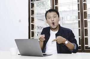 Young Asian man shocked and wow what he see in the laptop. photo