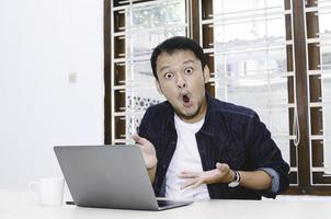 Young Asian man shocked and wow what he see in the laptop. photo