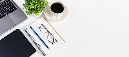 Laptop, coffee cup, tablet, and vase on white table in an office. Concept automation office using technology, network, internet. Copy space on right for a design, Close up, slope view white background photo