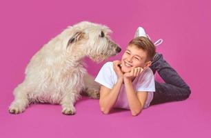 Smiling cheerful eleven years teen in white t-shirt and jeans with white Irish Wolfhounds on fuchsia color background in photo studio