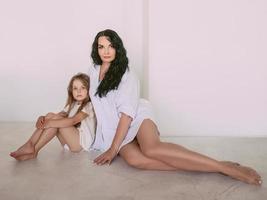 beautiful stylish brunette woman with adorable daughter sitting on the floor indoor. Family, love, style, fashion, support concept photo