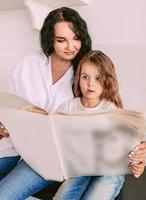 hermosa mujer morena con estilo con una hija adorable leyendo noticias de última hora en un periódico de papel. familia, periódico, noticias, conmoción, amor, concepto de apoyo foto