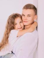 caucasian happy adorable siblings - teenager boy brother and little girl sister cuddling on white background indoor. Family, relationships, relatives, love, support concept photo