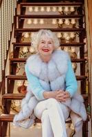 senior stylish woman in fur coat and with grey hair sitting and enjoying life. Travel, fashion,  fun, happiness, elderly age, seasonal concept photo