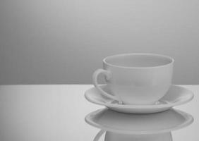 one white cup and saucer on a light background with reflection photo