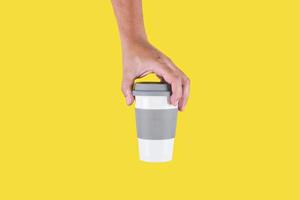 Hand holding a plastic cup of coffee to go in a yellow background photo