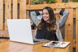 mujer relajada con las manos detrás de la cabeza en la mesa con portátil foto