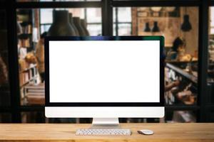 monitor de computadora, teclado, teléfono inteligente de taza de café, tableta y mouse con pantalla en blanco o en blanco aislado está en la mesa de trabajo en el café foto