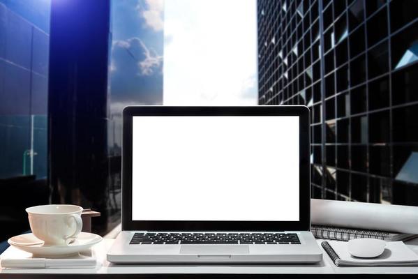 Front view of cup and laptop, smartphone, and tablet on table in office and background