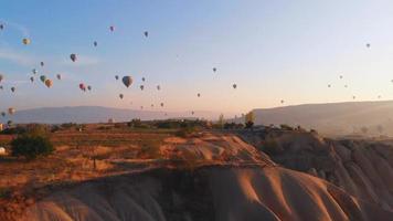 flygfoto stigande utsikt natursköna Kappadokiens dalar panorama med luftballonger i majestätisk blå himmel vid soluppgången video