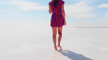 terug tracking weergave vrouwelijke vrouw blootsvoets in rode jurk lopen en verkennen van het witte tuz-zoutmeer in centraal anatolië, turkije video