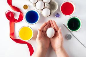 Young woman draws with colorful paints on white eggs for Easter. photo