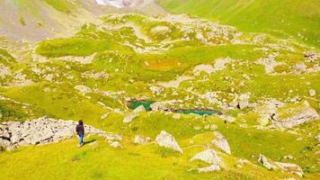 rastreamento aéreo vista traseira feminino caucasiano pessoa caminhar em direção à borda desfrutando de vistas de lagos glaciares kazbegi ao ar livre na natureza. video