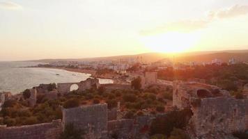 zoom panorâmico aéreo para câmera lenta ruínas históricas do castelo kiz kalesi na costa de mersin com panorama de fundo do pôr do sol video