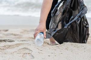 Woman cleans up by picking up plastic bottles at the beach. Concept of protecting the environment, saving the world, recycling, reducing global warming. closeup, blurred background, copy space on left photo