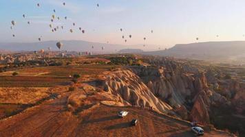 luchtfoto vogels eye view toerist op gezichtspunt kijken heteluchtballonnen in de lucht bij zonsopgang in cappadocië. Turkije reisbestemming 4k verkennen concept video