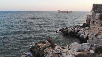 luchtfoto vrouwelijke persoon op rots neemt selfie met uitzicht op zee en beroemde toeristische bezienswaardigheid kiz kalesi kasteel aan de mediterrane kust in de zomer video