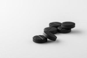 varias pastillas de carbón activado médicas negras sobre fondo blanco. aislado foto