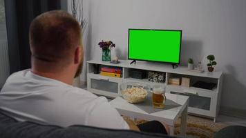 hombre viendo televisión de pantalla verde en casa.