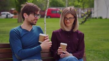Two friends with glasses, sit on the bench while sipping coffee to-go Coffee Break work Wearing Casual style. video
