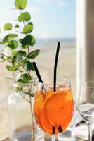 aperol spritz y ramitas de eucalipto en un jarrón sobre la mesa en un café en la playa cerca del mar en el día soleado foto