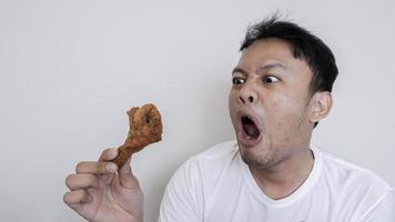 Shock and Wow face of Young Asian man is eating fried chicken wear white shirt. photo