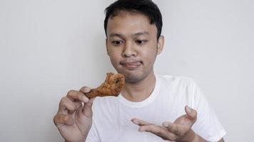 Young Asian man is eating fried chicken wear white shirt feeling tempted and hungry. photo