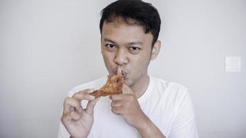 un joven asiático está comiendo pollo frito con camisa blanca con un gesto de mano silencioso. foto