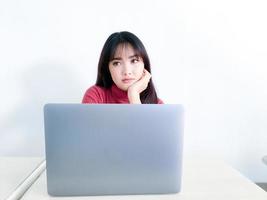 la chica de cabello hermoso asiático está confundida o aburrida en la parte delantera de la computadora portátil en el fondo blanco aislado foto