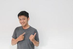 Wow and surprised face with smile of young Asian man in gray t-shirt with hand point on empty space. photo