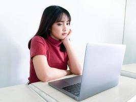 la chica de cabello hermoso asiático está confundida o aburrida en la parte delantera de la computadora portátil en el fondo blanco aislado foto
