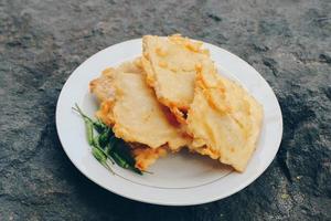 Tempe Mendoan is a type of tempeh dish made from thin tempeh, and fried in flour so that it tastes tasty and crunchy with soy sauce in wooden plate isolated on white background. photo