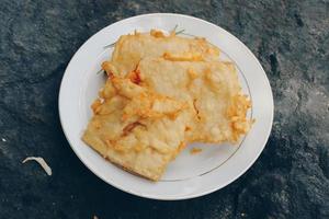 Tempe Mendoan is a type of tempeh dish made from thin tempeh, and fried in flour so that it tastes tasty and crunchy with soy sauce in wooden plate isolated on white background. photo
