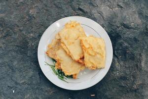 Tempe Mendoan is a type of tempeh dish made from thin tempeh, and fried in flour so that it tastes tasty and crunchy with soy sauce in wooden plate isolated on white background. photo